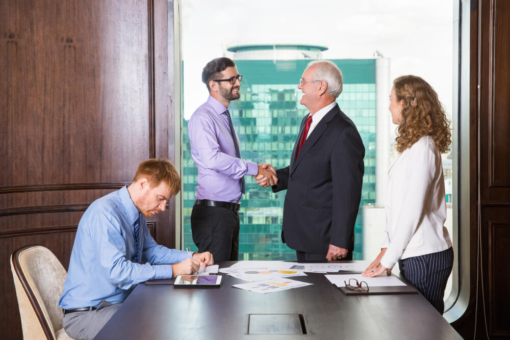 businessmen-shaking-hands-while-another-is-writing (1)
